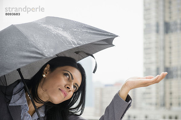 Indian businesswoman feeling rain from under umbrella