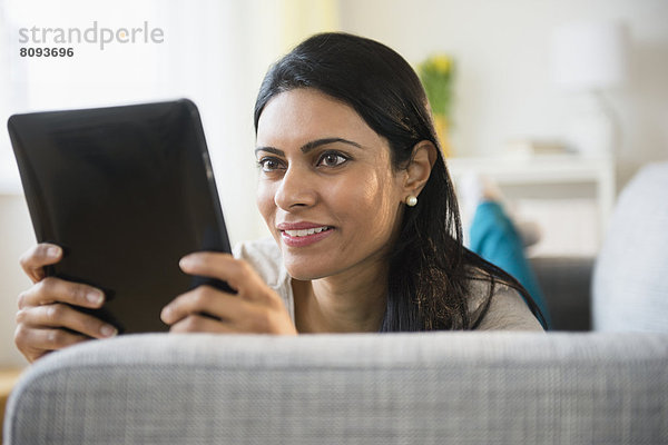 Indian woman using tablet computer on sofa