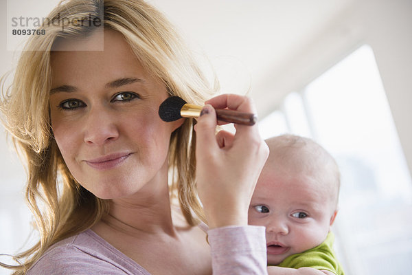 Caucasian mother with baby applying makeup