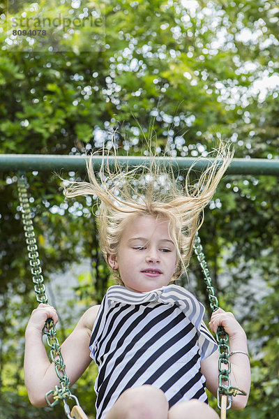 Caucasian girl playing on swing in park