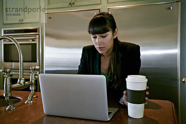 Mixed race businesswoman using laptop in kitchen