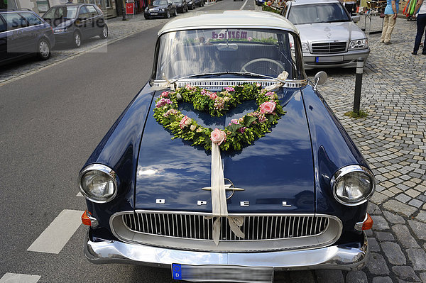 Blauer Opel Rekord P1 als Hochzeitswagen mit Blumenschmuck auf dem Kühler