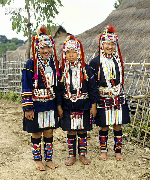 Drei Akha-Mädchen in einem Bergdorf mit traditioneller Kleidung und Kopfbedeckung