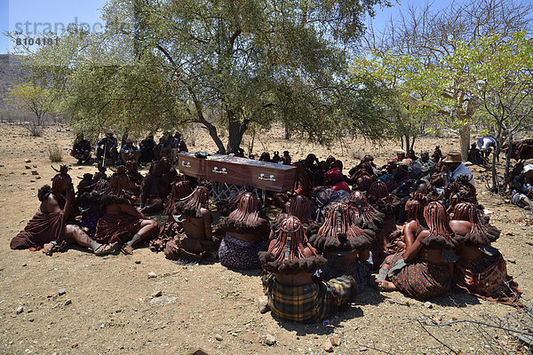 Trauernde Himba-Frauen sitzen bei einer Beerdigung um den Sarg