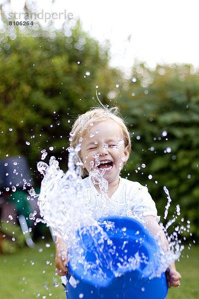 Blondes Mädchen spritzt mit Wasser im Garten