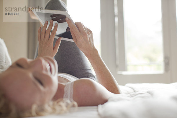Lachende Frau im Bett liegend mit digitalem Tablett