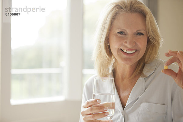 Porträt einer lächelnden Frau mit Pille und Wasserglas