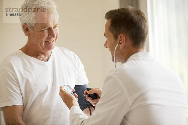 Arzt  der den Blutdruck des älteren Mannes im Büro des Arztes überprüft.