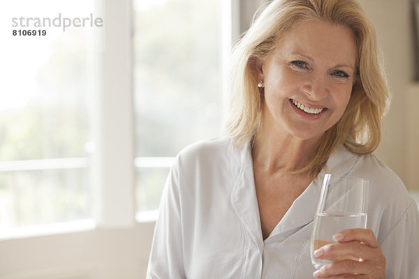 Porträt einer lächelnden Frau  die ein Glas Wasser trinkt.