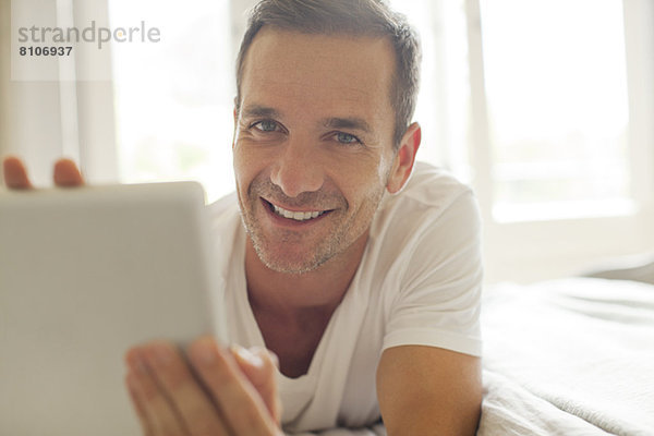 Porträt eines lächelnden Mannes mit digitalem Tablett im Bett