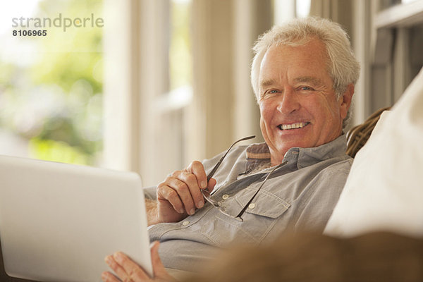 Porträt eines lächelnden älteren Mannes mit Laptop auf der Veranda