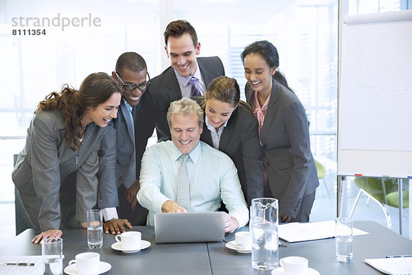 Lächelnde Geschäftsleute teilen sich den Laptop im Konferenzraum