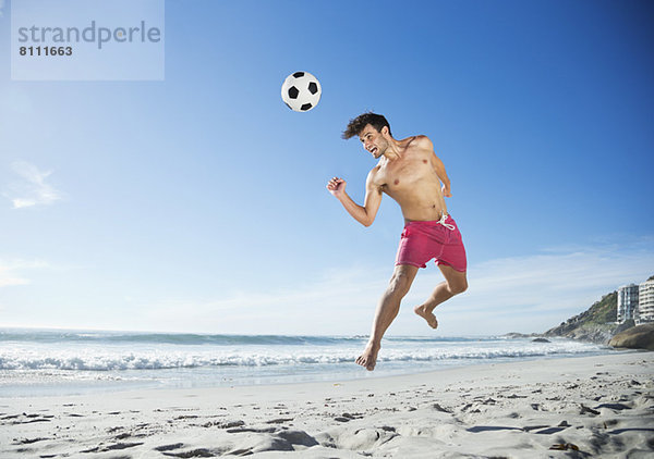 Mann in Badehose auf dem Weg zum Fußball am Strand