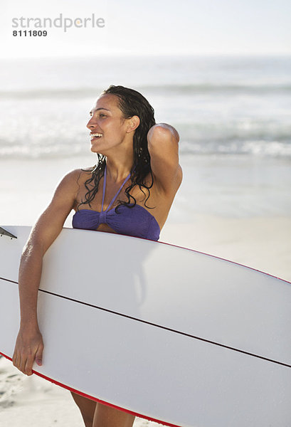 Lächelnde Frau mit Surfbrett am Strand