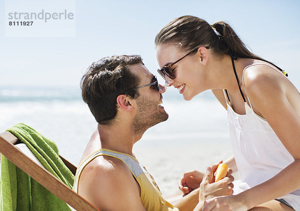 Ein glückliches Paar  das am Strand mit Sonnencreme bedeckte Nasen reibt.