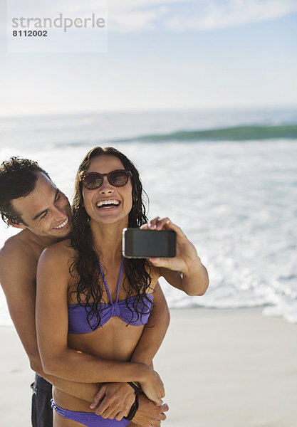 Glückliches Paar beim Selbstporträt mit Fotohandy am Strand