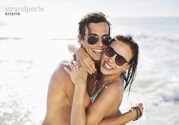 Porträt eines begeisterten Paares mit Sonnenbrille am Strand