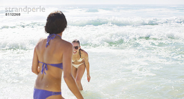 Glückliche Freunde in Bikinis beim Spielen im Meer