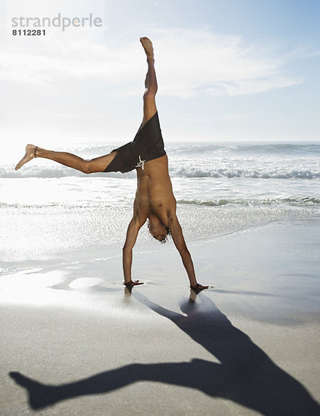 Mann in Badehose beim Handstand am Strand