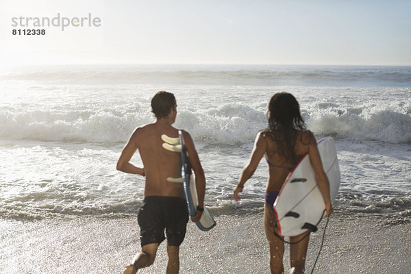 Paar läuft mit Surfbrettern in Richtung Ozean