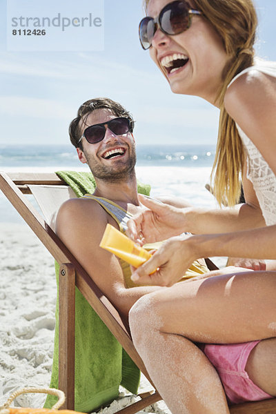 Glückliches Paar mit Sonnencreme am Strand