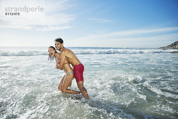 Enthusiastisches Paar  das sich umarmt und im Meer plätschert.