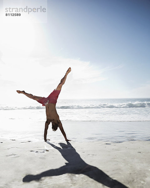 Mann in Badehose beim Handstand am Strand