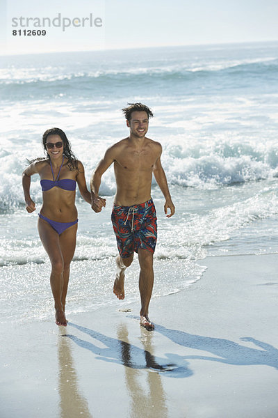 Ein glückliches Paar  das Händchen hält und am Strand rennt.