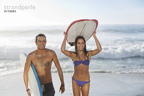 Glückliches Paar mit Surfbrettern am Strand
