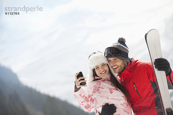 Glückliches Paar mit Skiern beim Selbstporträt mit Fotohandy