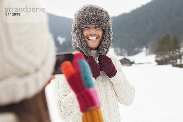 Frau fotografiert Mann mit Pelzmütze im Schneefeld