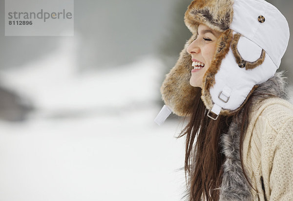 Glückliche Frau mit Fellmütze im Schnee