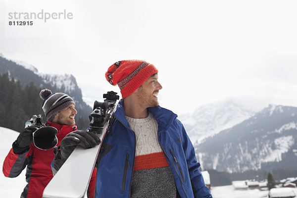 Lächelnde Männer mit Skiern am Fuße des Berges