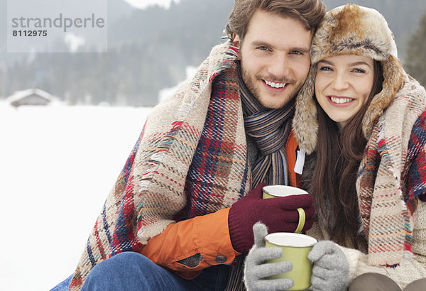 Porträt des glücklichen Paares beim Kaffeetrinken im verschneiten Feld