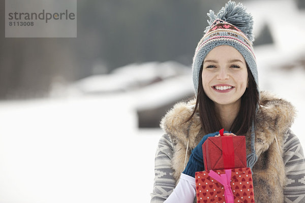 Porträt einer lächelnden Frau mit Weihnachtsgeschenken im Schneefeld