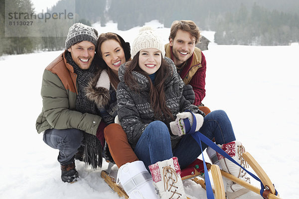 Porträt von glücklichen Freunden auf dem Schlitten im Schneefeld
