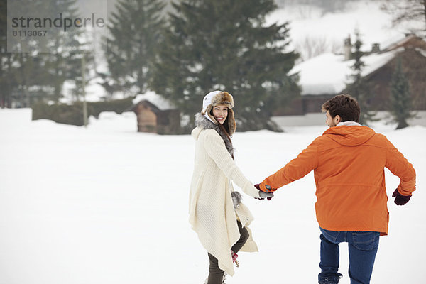 Ein glückliches Paar hält sich an den Händen und geht in einem verschneiten Feld spazieren.