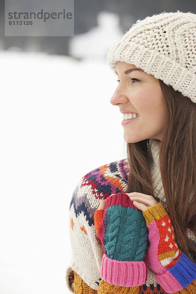 Nahaufnahme einer lächelnden Frau mit Strickmütze und fingerlosen Handschuhen im Schneefeld
