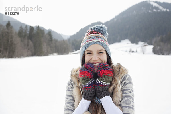 Porträt einer begeisterten Frau mit Strickmütze und Handschuhen im Schneefeld
