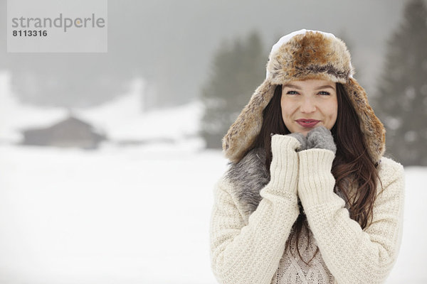 Porträt einer lächelnden Frau mit Pelzmütze und Handschuhen im Schneefeld