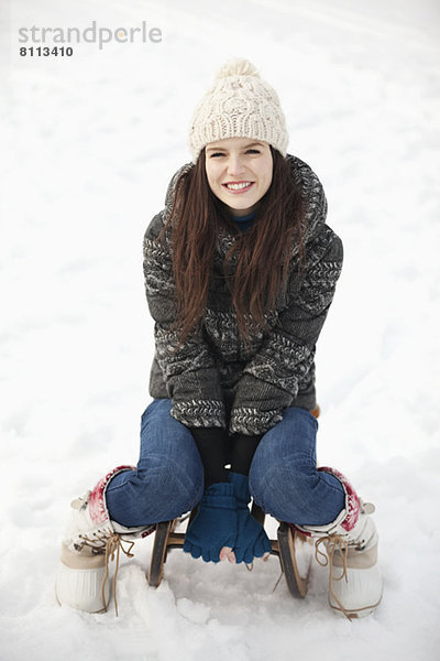 Porträt einer lächelnden Frau  die auf einem Schlitten im Schnee sitzt.