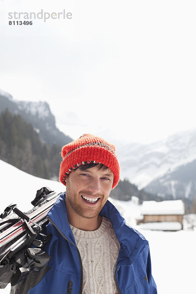 Nahaufnahme des lächelnden Mannes mit Skiern im Schneefeld