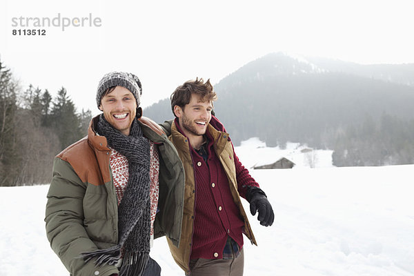 Porträt von glücklichen Männern  die im verschneiten Feld spazieren gehen.