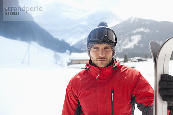 Porträt eines selbstbewussten Mannes mit Skiern im Schneefeld