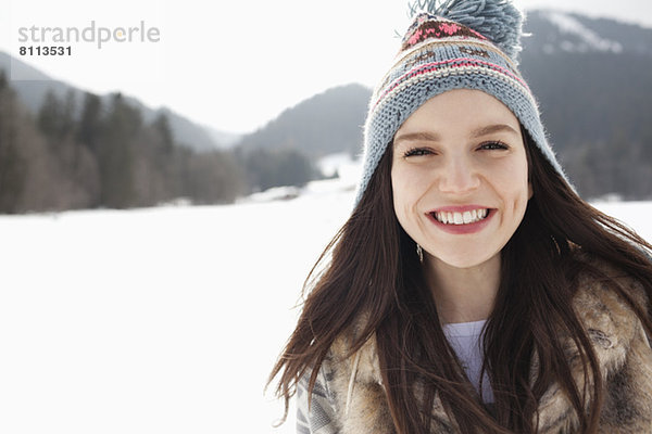 Nahaufnahme Porträt einer glücklichen Frau mit Strickmütze im Schneefeld