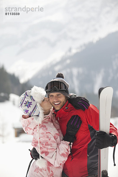 Glückliches Paar mit Skiküssen im Schneefeld