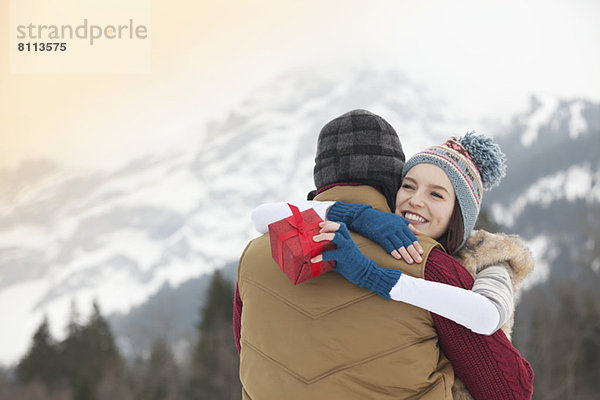 Glückliche Frau mit Geschenk und umarmendem Mann mit Bergen im Hintergrund