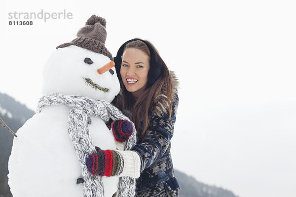 Porträt einer fröhlichen Frau  die den Schneemann umarmt