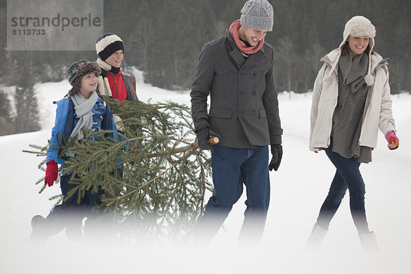 Glückliche Familie mit frischem Weihnachtsbaum im Schneefeld
