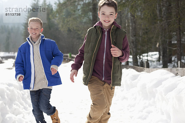 Porträt der glücklichen Jungen  die in der verschneiten Gasse rennen